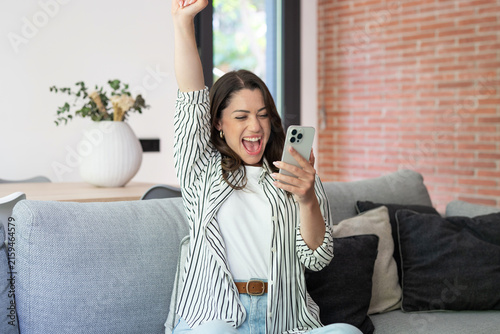 Konstfotografi Woman sitting on a sofa expressing joy and celebrating success while looking at