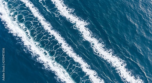 Aerial top down view of white foam boat wake trails across deep blue ocean water