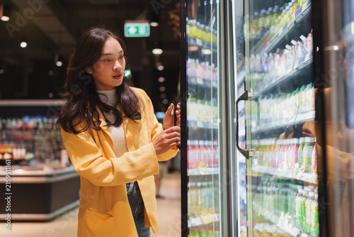 Woman choosing drinks from supermarket refrigerator in grocery store