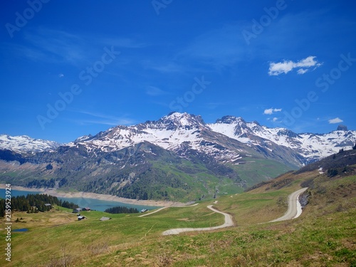 Panoramic view of Roselend Lake with snowy Alpine peaks, green hills, hiking trails and evergreen forest, haking 