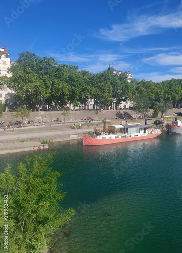Lyon,France-Juin 14,2026:Barge sailing on the Rhone River,viewed from a bridge with crystal clear blue water and urban skyline