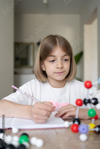 Young girl scientist studying molecular model in a home, carefully examining the structure. STEM education