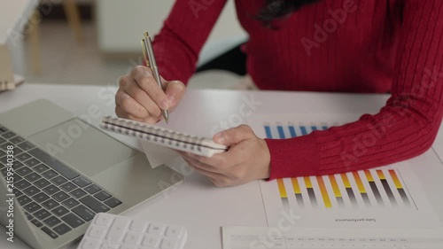 Businesswoman writing notes and analyzing financial charts at office desk