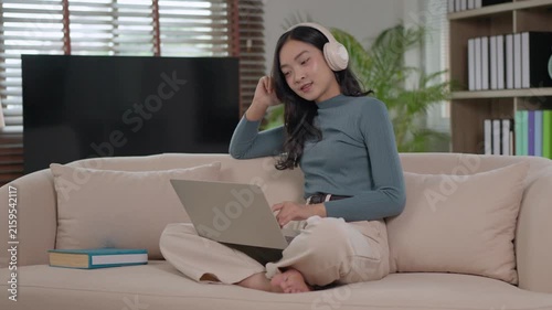 Young asian woman enjoying music while working on laptop