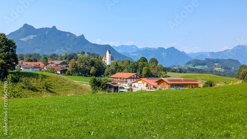 A picturesque Alpine landscape in the Chiemgau Pre-Alps, with green meadows and the idyllic village setting of Grainbach am Samerberg against an imposing mountain range in Bavaria, Germany