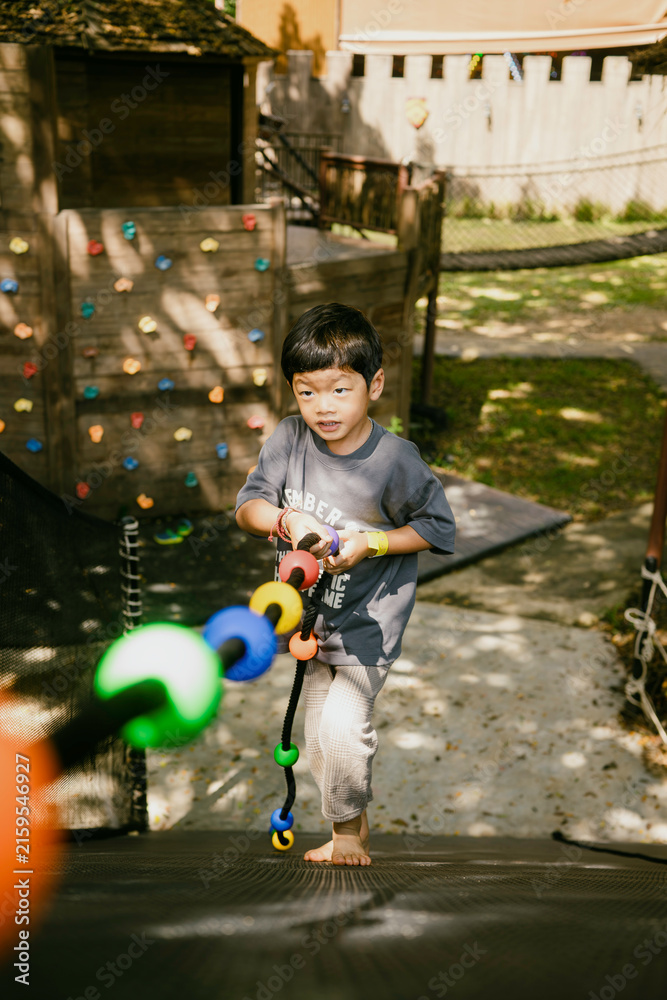 Fototapeta premium Young child pulling a colorful rope on an outdoor playground, developing strength, grip, balance and coordination through active physical play and adventure.