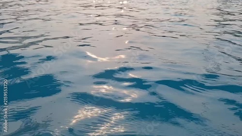 Close-up of calm blue swimming pool water with sparkling golden sunlight reflections and gentle waves.