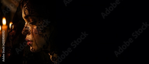 Close up profile of beautiful young woman face covered in black lace veil mantilla under warm candle lighting, luxury gothic fashion and dark moody conceptual fine art with large copy space