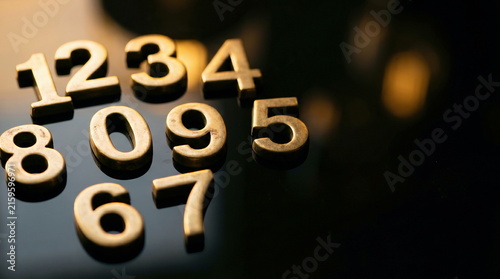 Digits, golden metallic numbers scattered on reflective black surface, representing education, data, and technology.