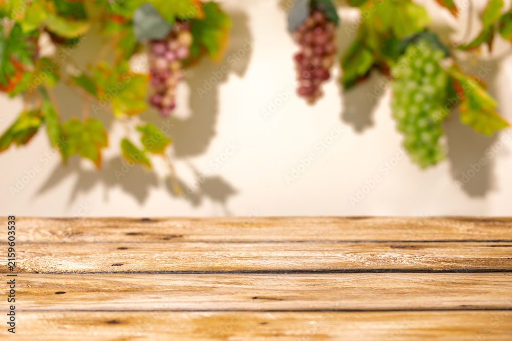 Naklejka premium Wooden table with blurred grape bunches and vine leaves as autumn harvest mockup background