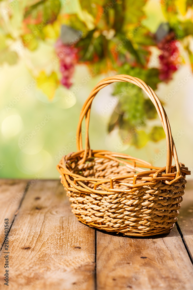 Naklejka premium Wicker basket on wooden table with blurred grapevine background for rustic autumn harvest product scene