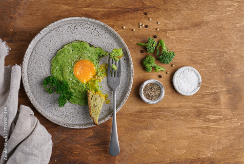 Fried egg with broccoli puree on a plate with bread and spices on wooden background