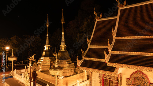 Canvas Print Phra That Doi Tung rises above the dark highland landscape, its radiant golden architecture contrasting with the forest and distant lights in a serene aerial scene from 2023