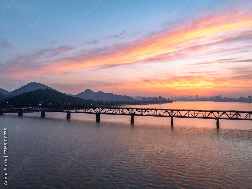 Obraz premium Bridge spanning river with sunset sky and distant mountains