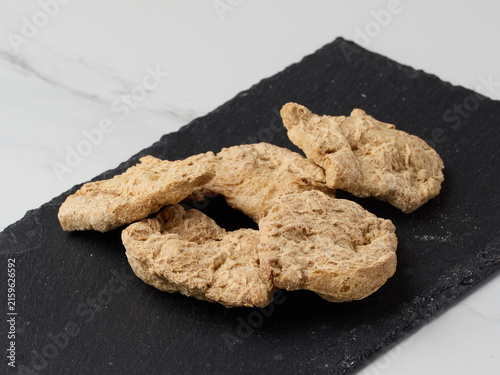 A top-down, close-up shot of raw, dehydrated soy meat pieces (textured vegetable protein cutlets) arranged on a dark, textured slate board against a light marble background.