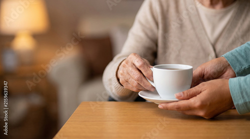 Caregiver or volunteer serving hot cup of tea to senior woman at home, hands of nurse giving warm drink to elderly patient showing care empathy and compassion in nursing home
