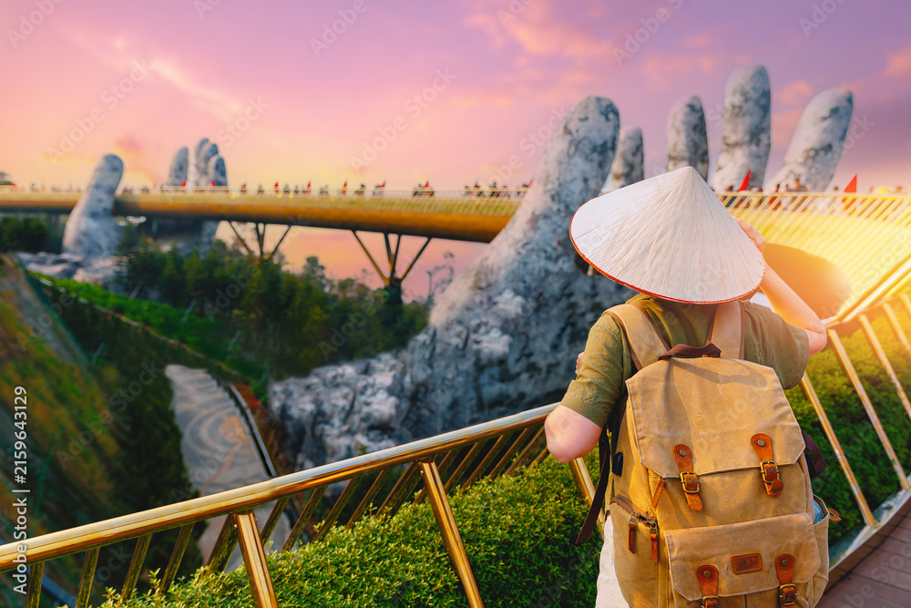 Fototapeta premium Tourist with straw hat and backpack admiring golden bridge at ba na hills, Da nang Vietnam