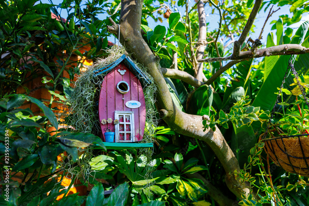 Naklejka premium Whimsical pink birdhouse hanging in a lush garden
