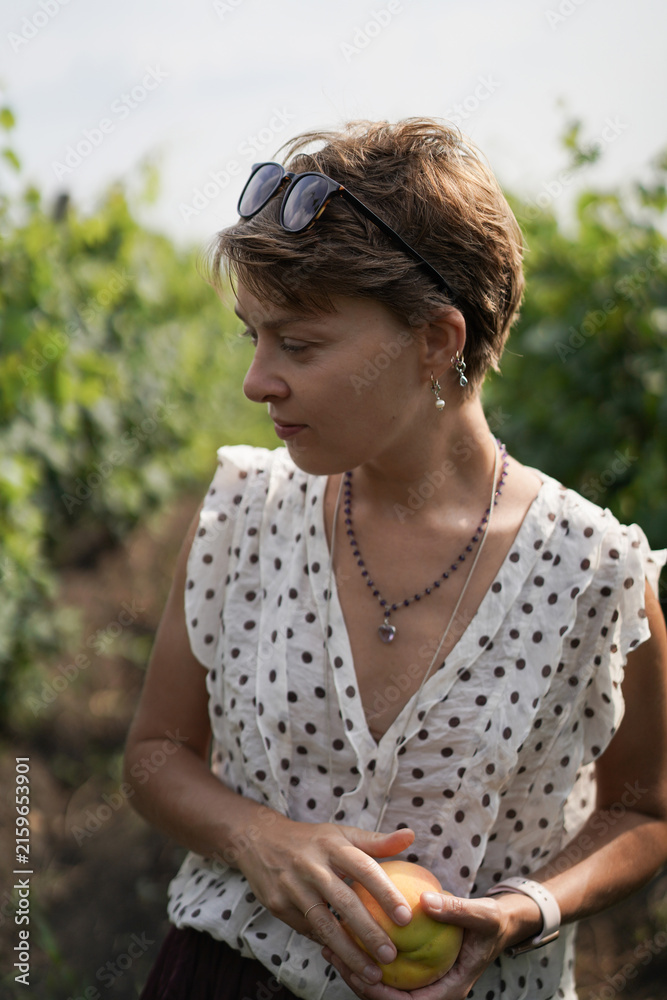 Naklejka premium Thoughtful woman holding a ripe peach in a garden