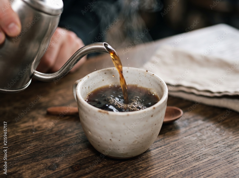 Fototapeta premium Pouring hot black coffee from a gooseneck kettle into a rustic ceramic mug on a wooden table