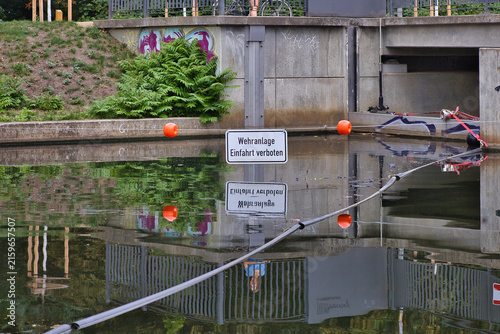 Warnschild an der Wehranlage des Blüthnerwehrs mit deutlicher Wasserspiegelung und Sicherheitsabsperrung am Kanal – Leipzig, Sachsen, Deutschland