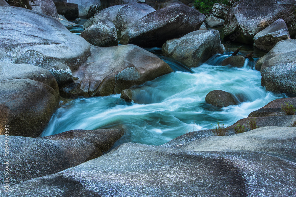 Fototapeta premium Clear turquoise mountain stream rushing over smooth granite rocks in a natural forest landscape