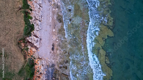 Obraz na plátně Aerial view of a serene coastline with gentle waves lapping against rocky cliffs and sandy beach