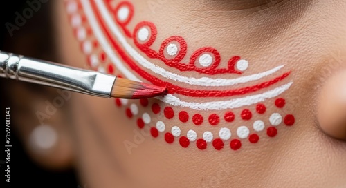 Face paint application detail using brush on cheek. Face paint includes intricate red white dot pattern, detailed makeup design, artistic lines. Cultural face paint serves as vibrant festive art.