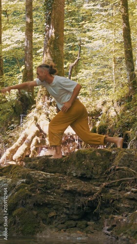 A man practices yoga on a moss-covered rock in a sunlit forest, balancing with focused precision. The serene environment enhances his meditative state, embodying a healthy lifestyle through nature.