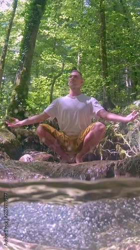 A young man sits cross-legged in a yoga pose, meditating in a lush, sunlit forest. His arms are outstretched, embodying balance and tranquility.