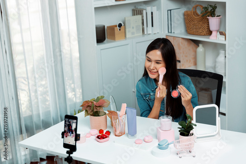 Принти на полотні Young beautiful Asian reviewing cosmetic makeup brush cheek testing collection with pastel color, showing glow blusher mood with pink to promote on social media online recording smartphone