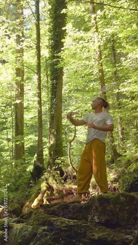 In a serene forest, a man practices yoga, balancing on rocky terrain amidst lush greenery. his focused movements and the tranquil environment highlight a moment of zen-like relaxation.