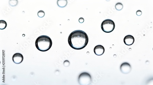 Clear water droplets of varying sizes suspended on a transparent surface against a white background.