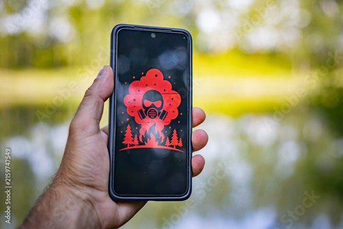 Man holding smartphone with severe air pollution warning icon on screen due to wildfires.