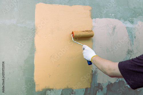Hand rolls paint over rough wall surface