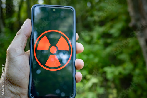 In the forest, a smartphone with a radiation hazard warning symbol in hand is a concept of environmental pollution.