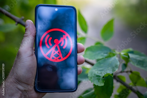 Man holding smartphone with no signal icon on screen in nature.
