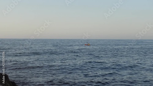 Man paddling kayak on ocean water waves in the distance cuts across the shot from right to left

