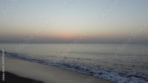 Seashore of sandy beach with waves coming in on a very calm Mediterranean Sea, with clear sky and horizon line, at dawn or dusk
