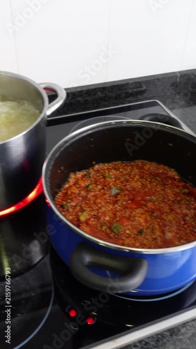 Vertical shot of two pots preparing pasta bolognese. One pot with the sauce and another with the pasta cooking. On a home electric stove
