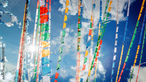 Foto Colorful Tibetan Prayer Flags Fluttering Against a Bright Blue Sky with Sunlight