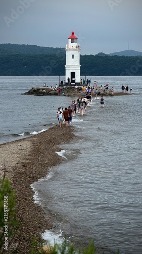 Photography Vladivostok Lighthouse on rocky shore with wooden posts leading into calm water,