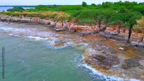Aerial view pans across rugged coastline with rolling waves crashing against ancient ruins, blending history with the serene seaside landscape.