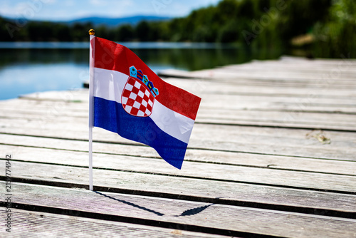 Fotografie Croatian flag with checkerboard coat of arms on weathered pier by a clear lake u