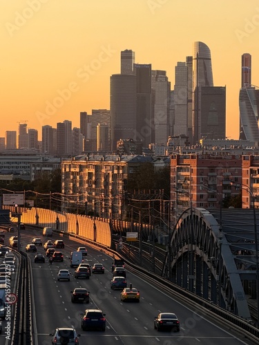 Moscow cityscape at sunset with a busy highway filled with cars, modern skyscrapers rising in the background, highlighting urban development and architecture