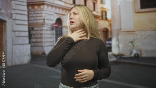 Foto Woman grasping throat with one hand and pressing her stomach while choking on a cobbled street; panic emergency help