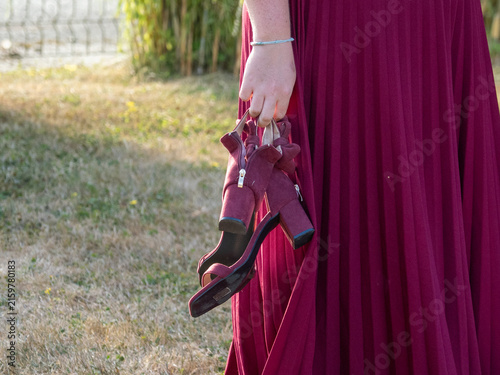 Canvastavla Femme en robe bordeaux tenant ses chaussures à talons à la main lors d’un mariag