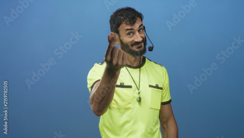 Obraz na płótnie Man referee wearing neon yellow shirt with whistle on lanyard and headset beckons with fingers toward camera in studio; confidence authority