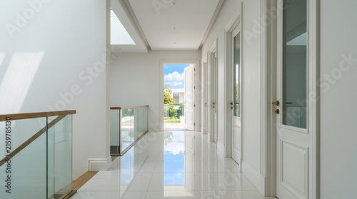 Modern hallway with glass railing, white walls, and natural light leading to garden