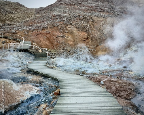 Iceland. Colorful geothermal landscape with steaming blue water and mineral-rich earth, showcasing a series of rocky formations and wooden walkways in a natural hot spring area
